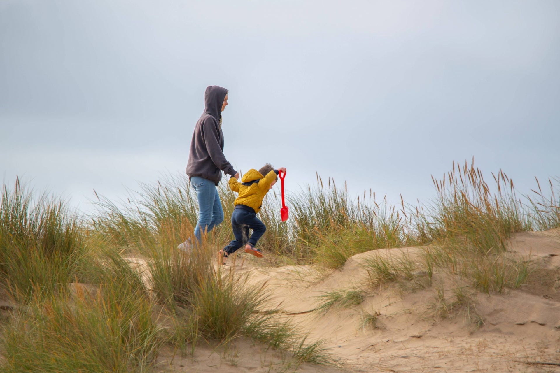 An adult and child walk along sandy dunes covered in tufts of grass.