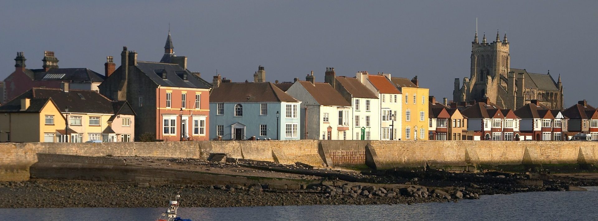 Colourful houses along a coastal seawall with a church in the background.