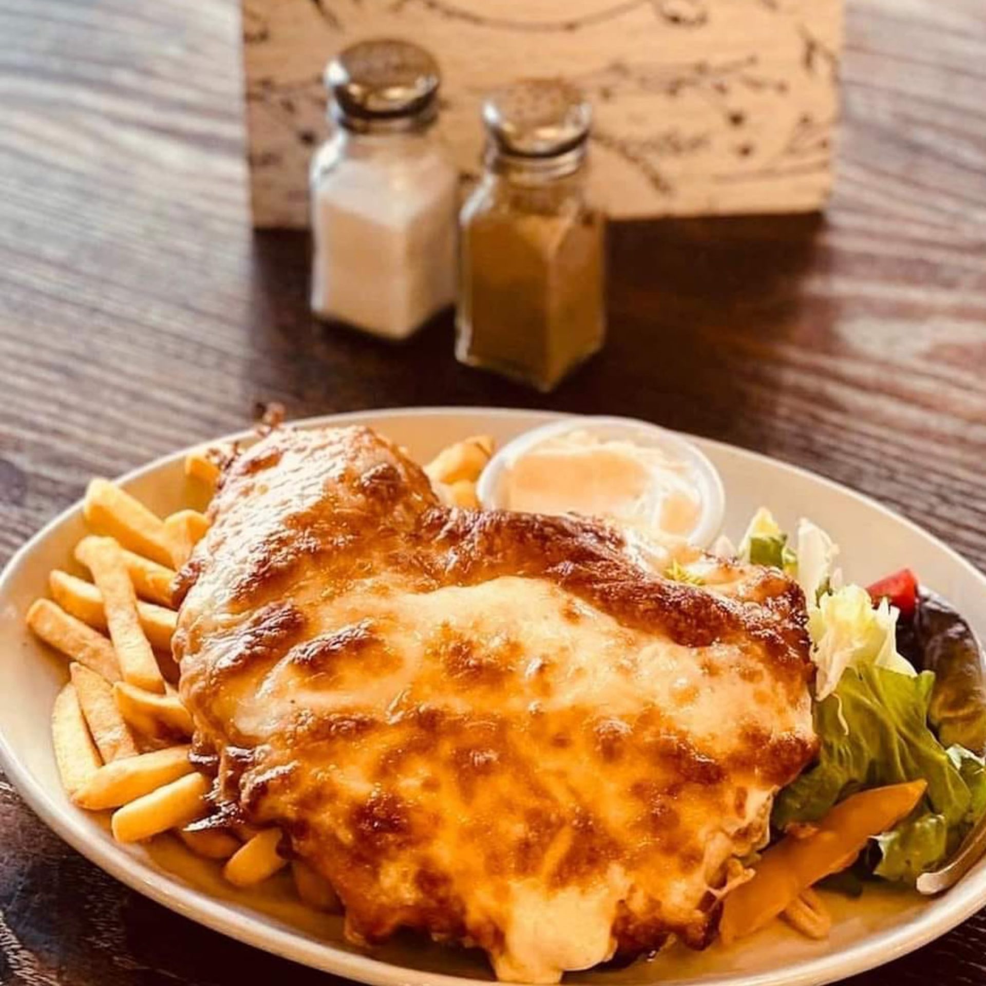 Chicken parmo with French fries and salad on a wooden table.