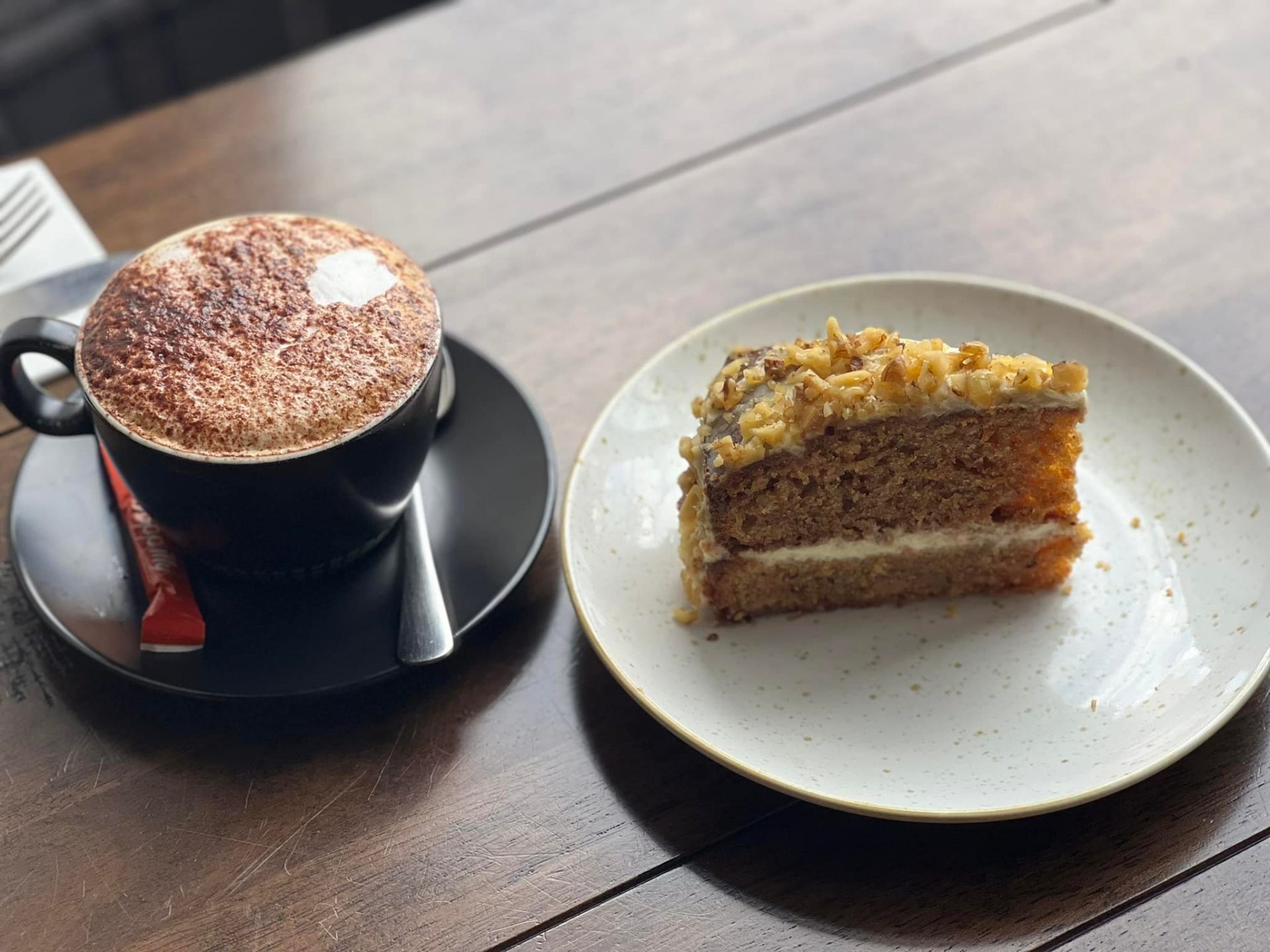 Cappuccino coffee next to a slice of walnut cake on a wooden table.