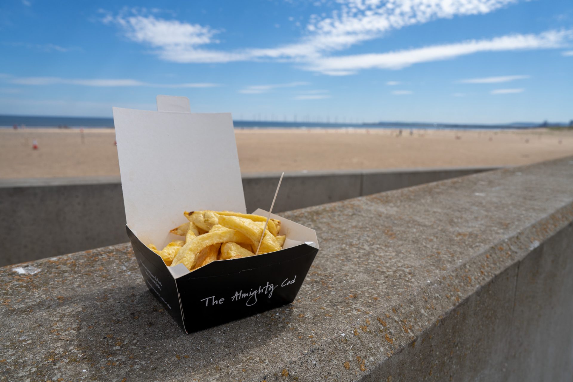 Takeaway box of chips with wooden fork on the a wall at the beach.