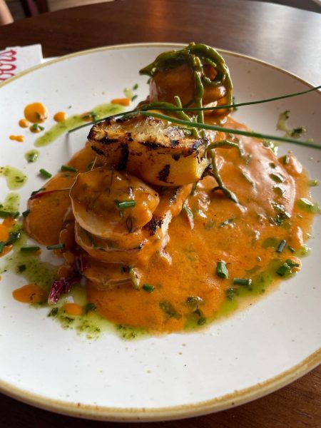 A plated gourmet dish featuring stacked chicken medallions topped with grilled lemon, green herbs, and a creamy orange sauce, garnished with chopped chives and green oil on a white plate.