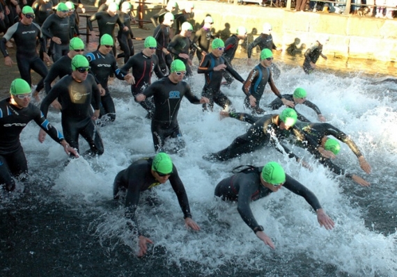Photo of a lot of people in wetsuits and green swim caps running and diving into Hartlepool Marina.