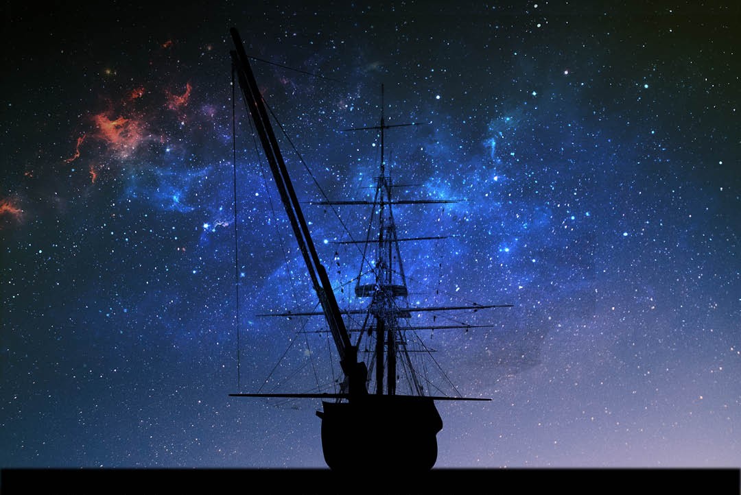 Silhouette of an old sailing ship with tall masts against a star-filled night sky with bright blue and orange nebulae.