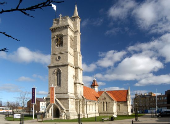 A stone church with a tall clock tower and arched entrance surrounded by grass.