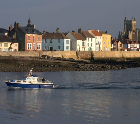 Colourful houses along a coastal seawall with a church in the background and small white sail boat.