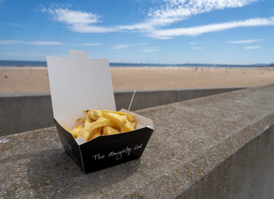 Takeaway box of chips with wooden fork on the a wall at the beach.